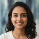Smiling South Asian woman in her late 20s or early 30s, her expression calm and content, against a soft blue and white backgr